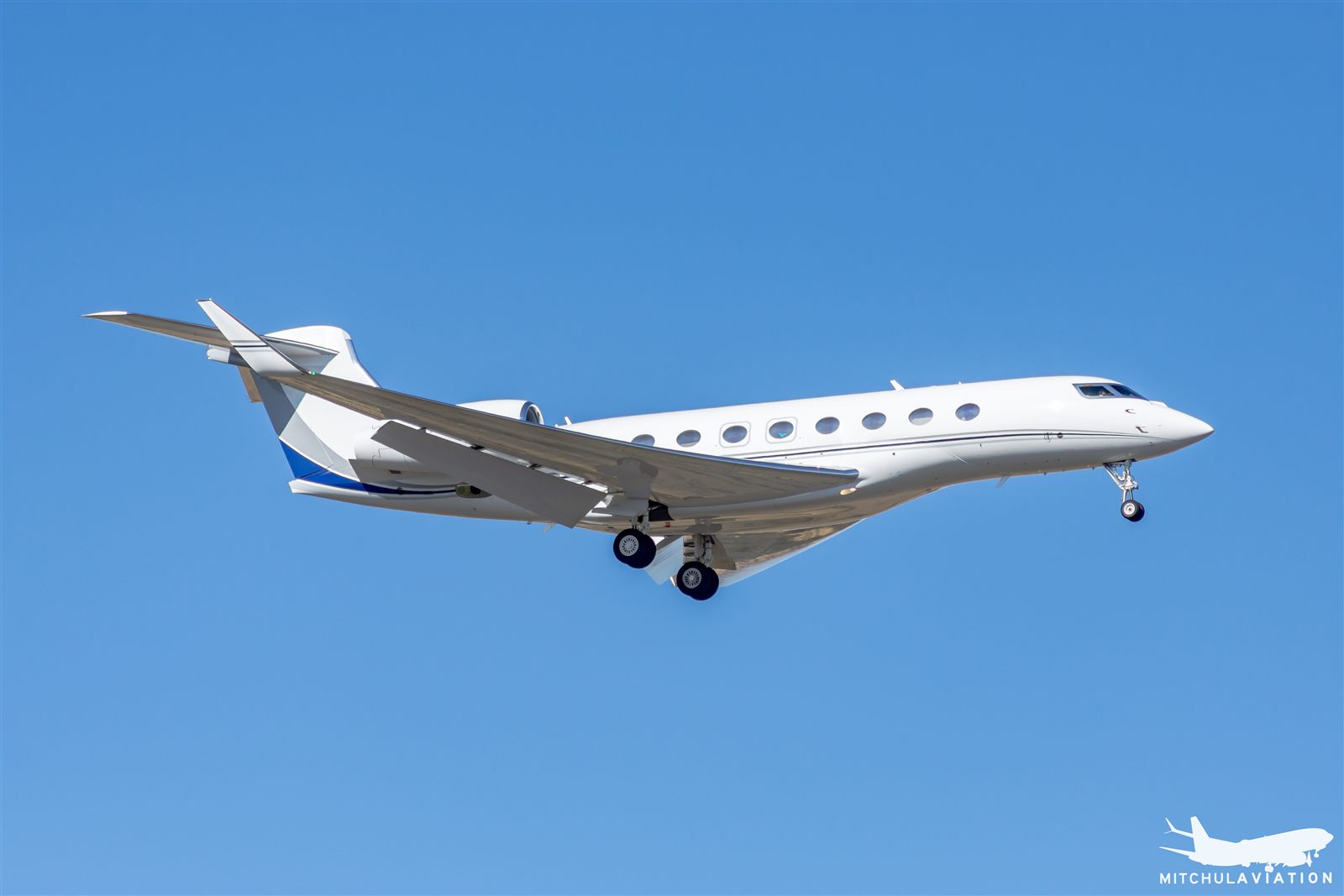 A Gulfstream G650 business jet banking in flight against a clear blue sky