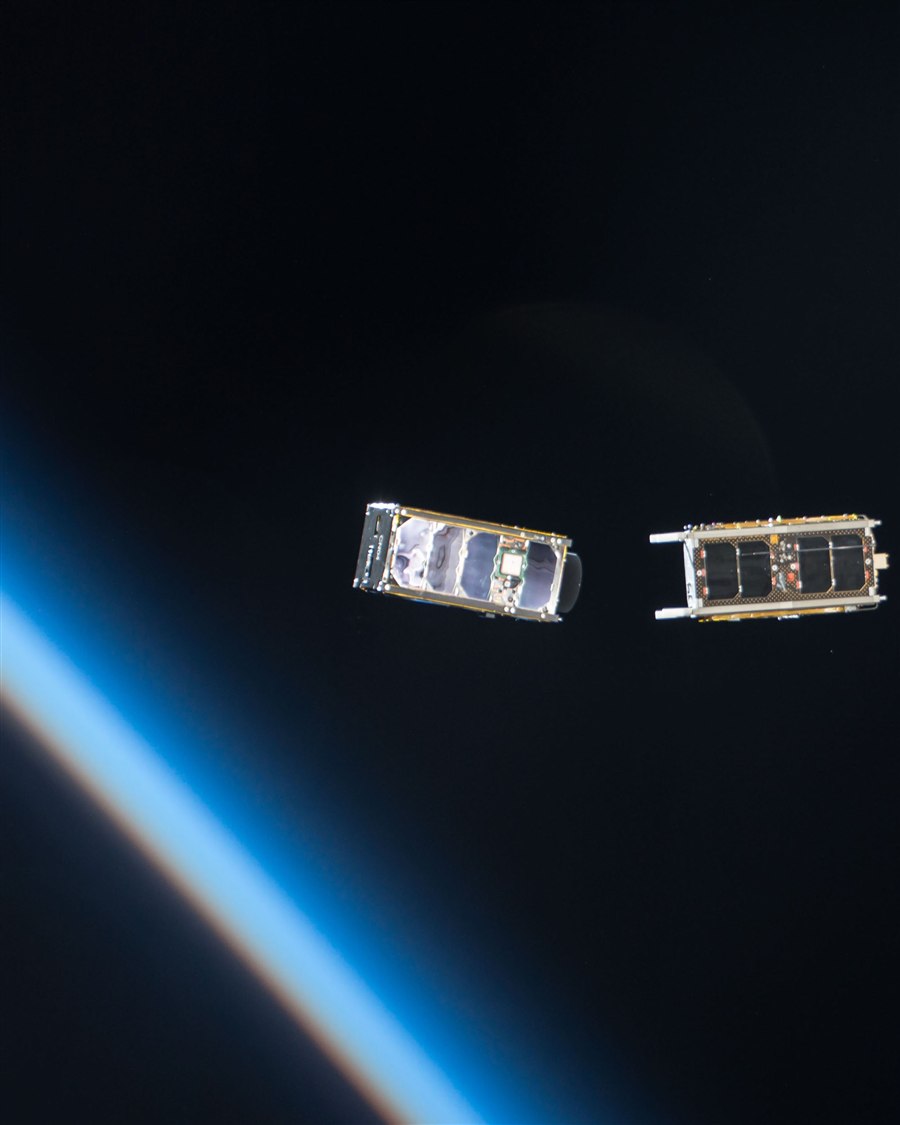 Two CubeSats freshly deployed from the International Space Station, floating against Earth's blue atmospheric limb